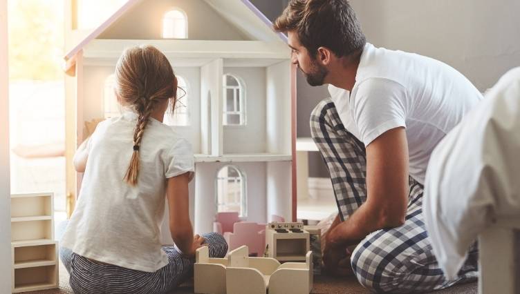Una bambina e un adulto che giocano con la casa delle bambole